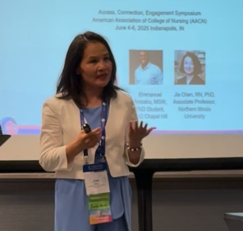 A woman, Lily Chen, in a white blazer speaks while holding a microphone and clicker. She stands in front of a projected presentation slide about a nursing symposium in Indianapolis, showing speaker names and photos.