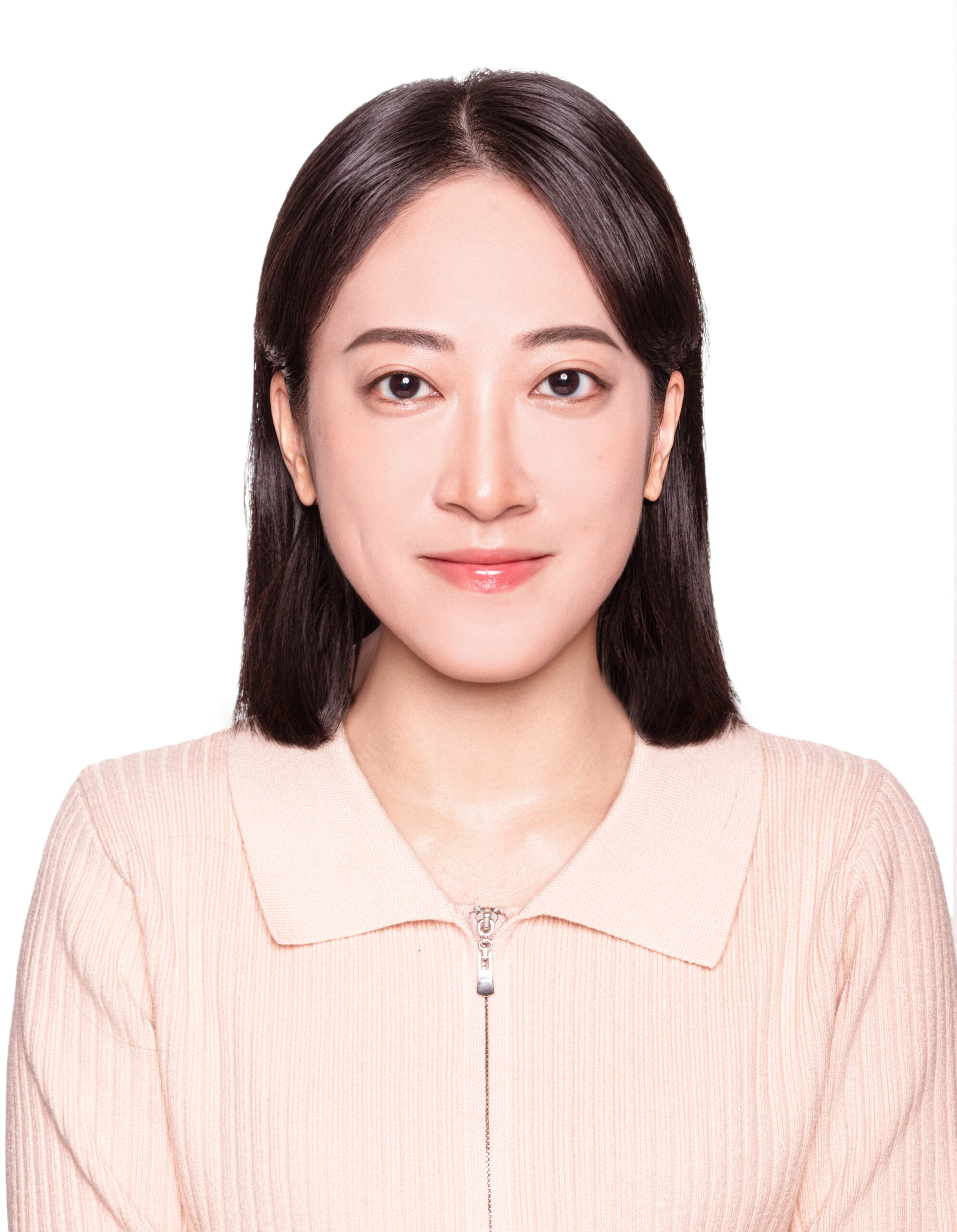 A woman with straight dark hair, wearing a pale pink ribbed zip-up top, is smiling softly at the camera against a plain white background.