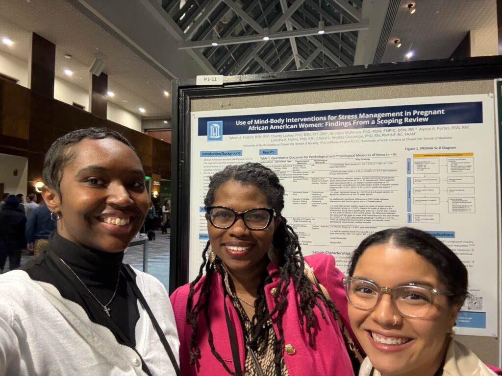 Three women smiling and posing in front of a scientific poster titled “Use of Mind-Body Interventions for Stress Management in Pregnant African American Women” at an indoor conference or event.