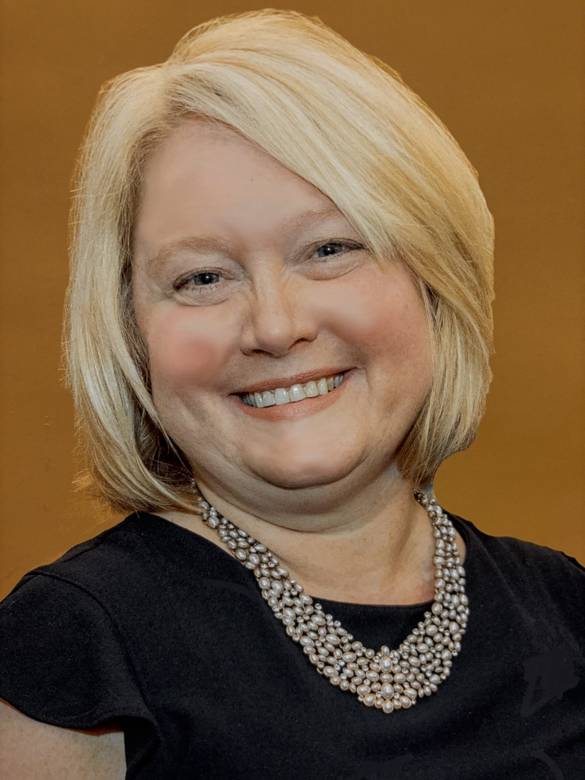 A woman with short blonde hair, wearing a black top and a pearl necklace, smiles at the camera against a plain orange background.