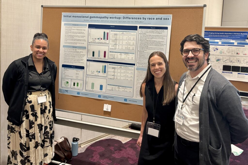 Three people stand smiling in front of a scientific research poster titled Initial monoclonal gammopathy workup: Differences by race and sex at a conference. Charts and data are visible on the poster behind them.